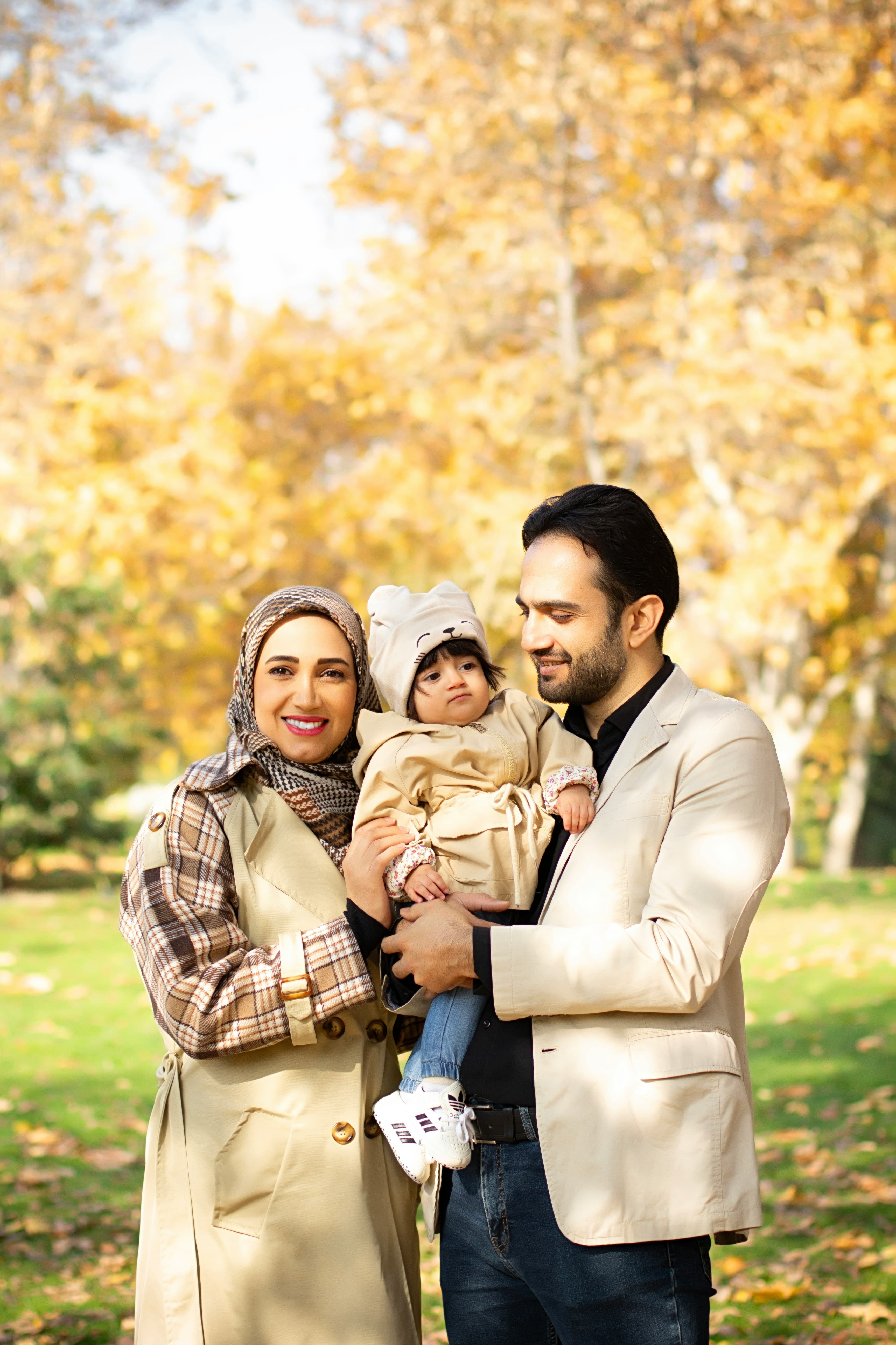 A smiling family with a young child standing together in an autumn park