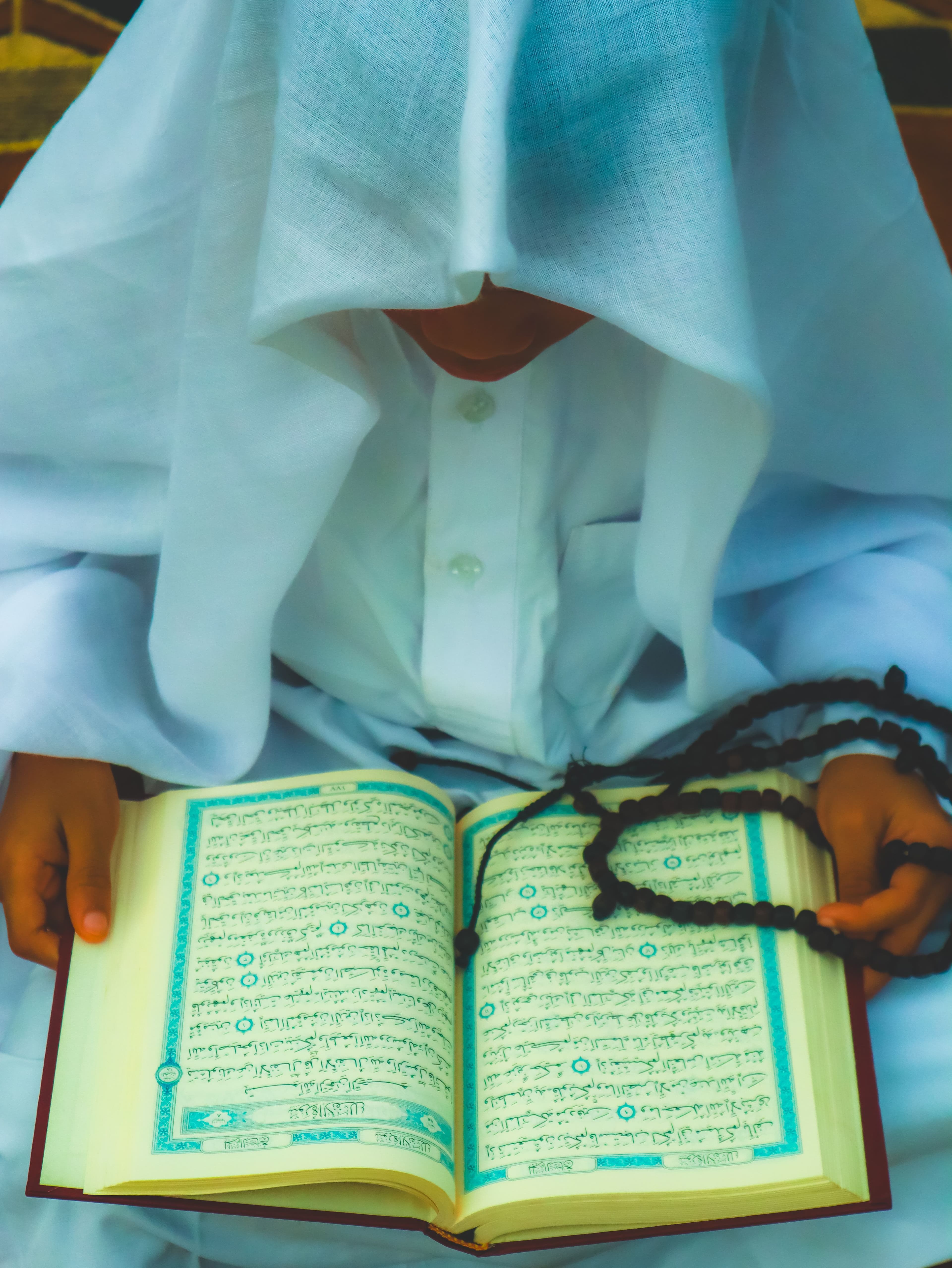 A student holding the Quran and tasbih beads during memorization practice