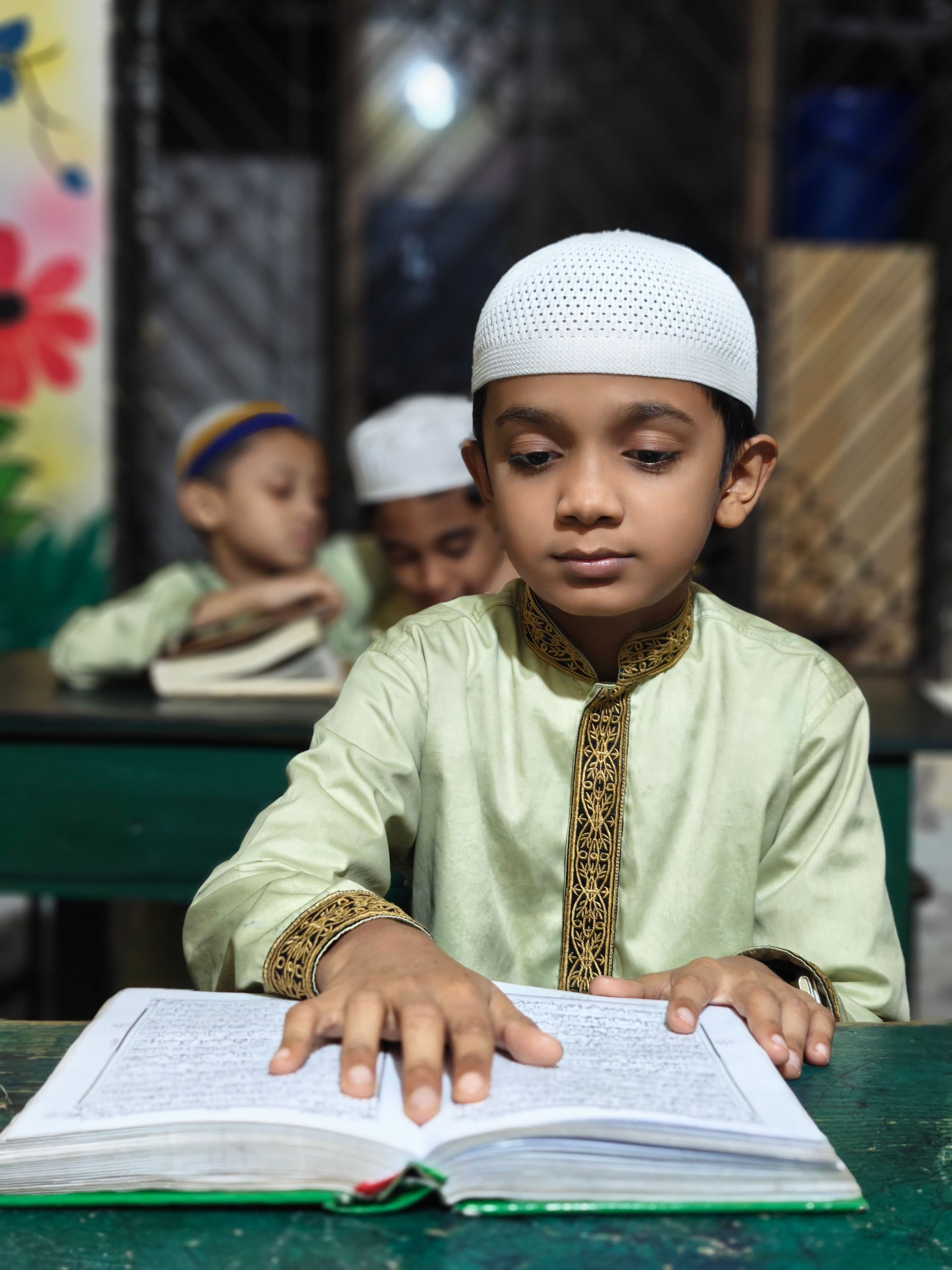 A young student reading from an open Arabic primer during class