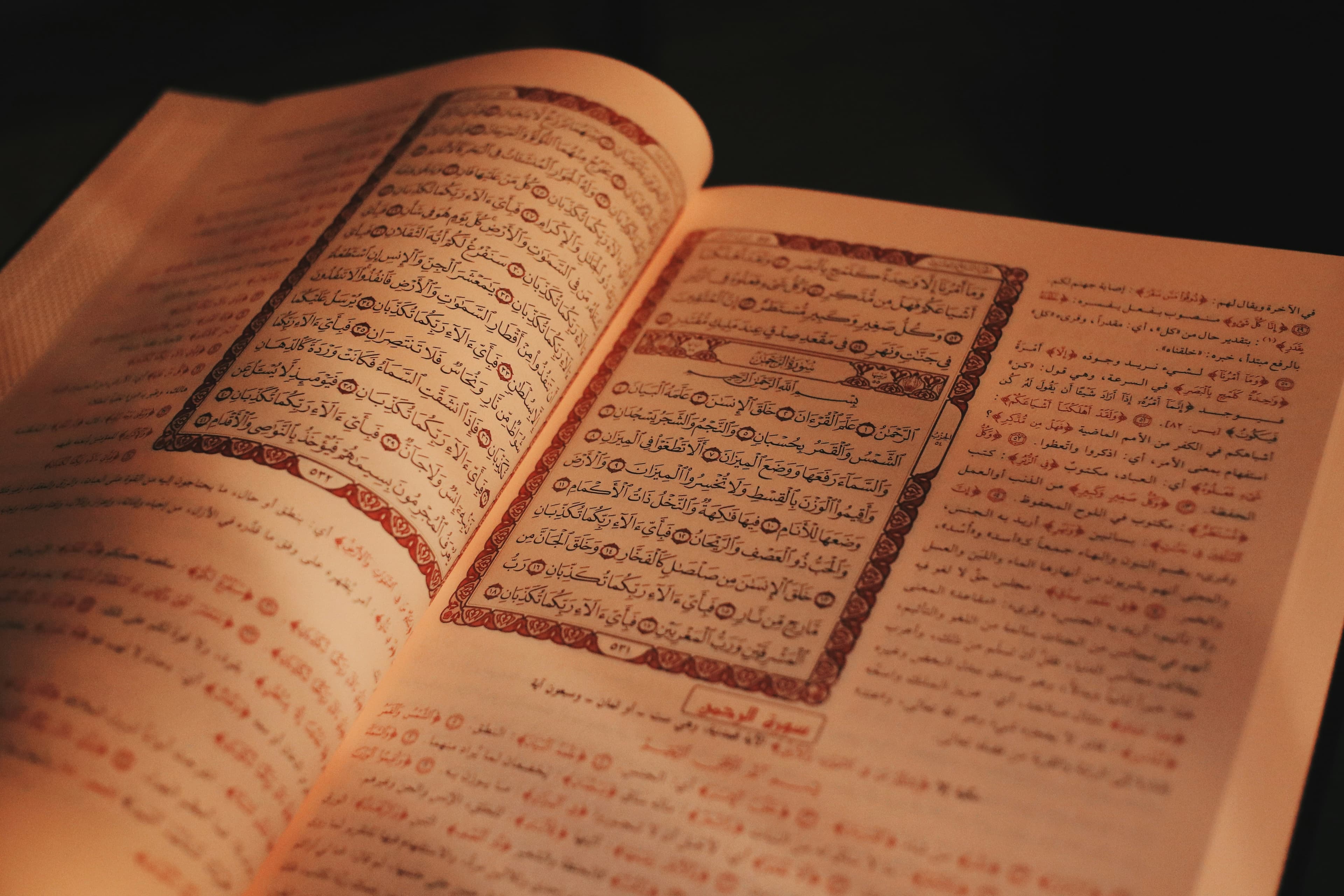 An open Quran with Arabic calligraphy and red ornamental borders, lit by warm light