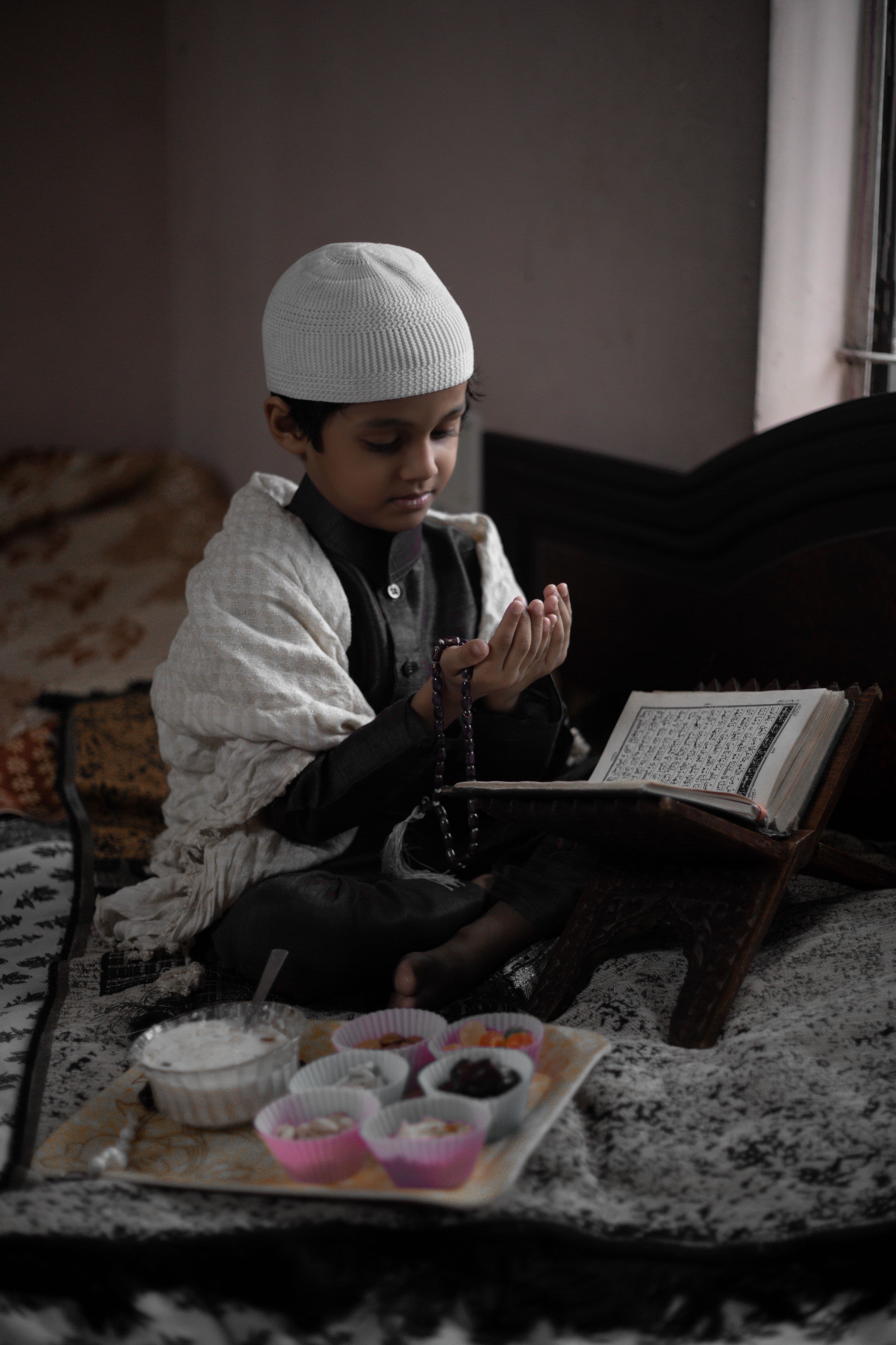 A young boy making dua in front of an open Quran
