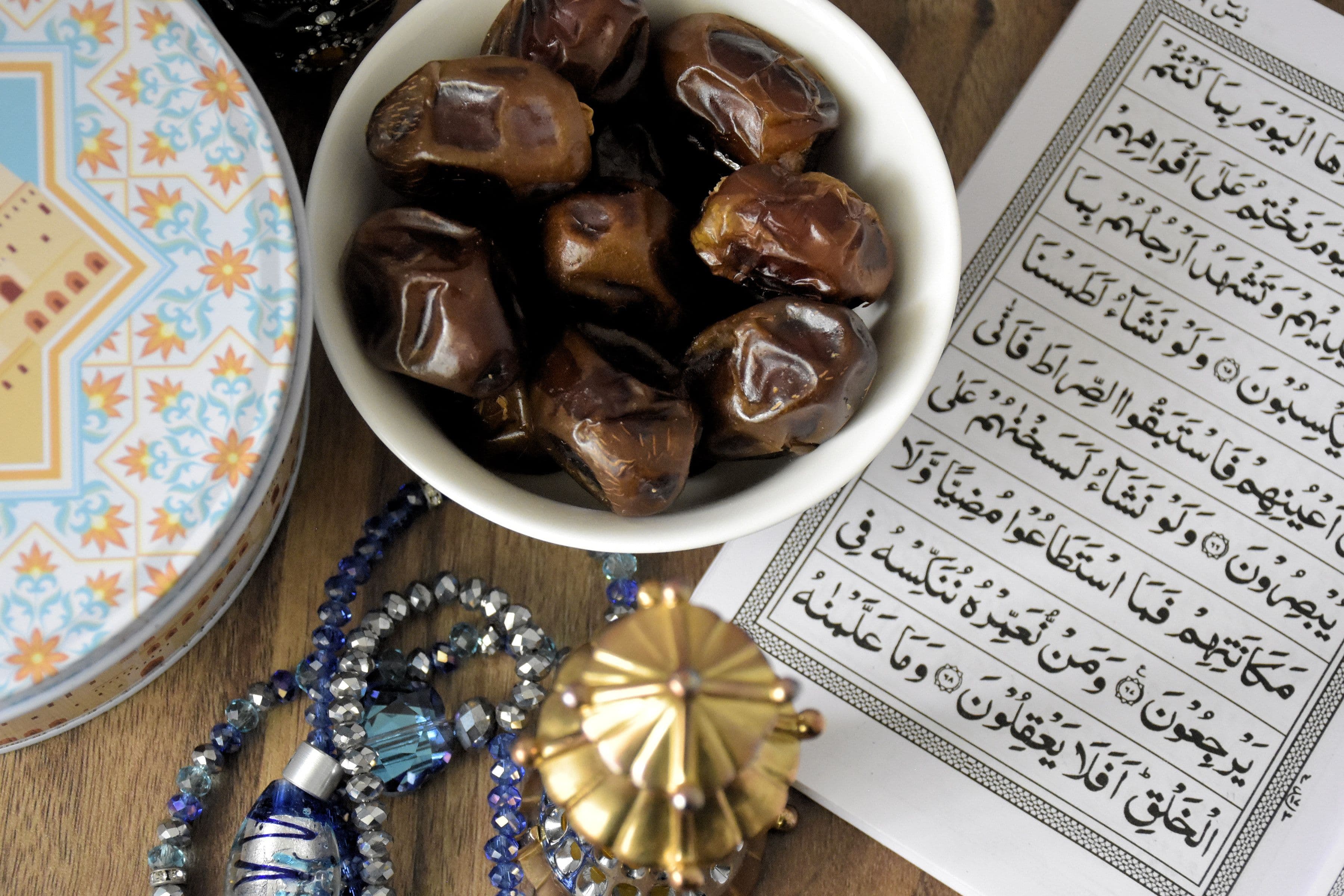 A bowl of dates beside an open Quran and prayer beads on a wooden table