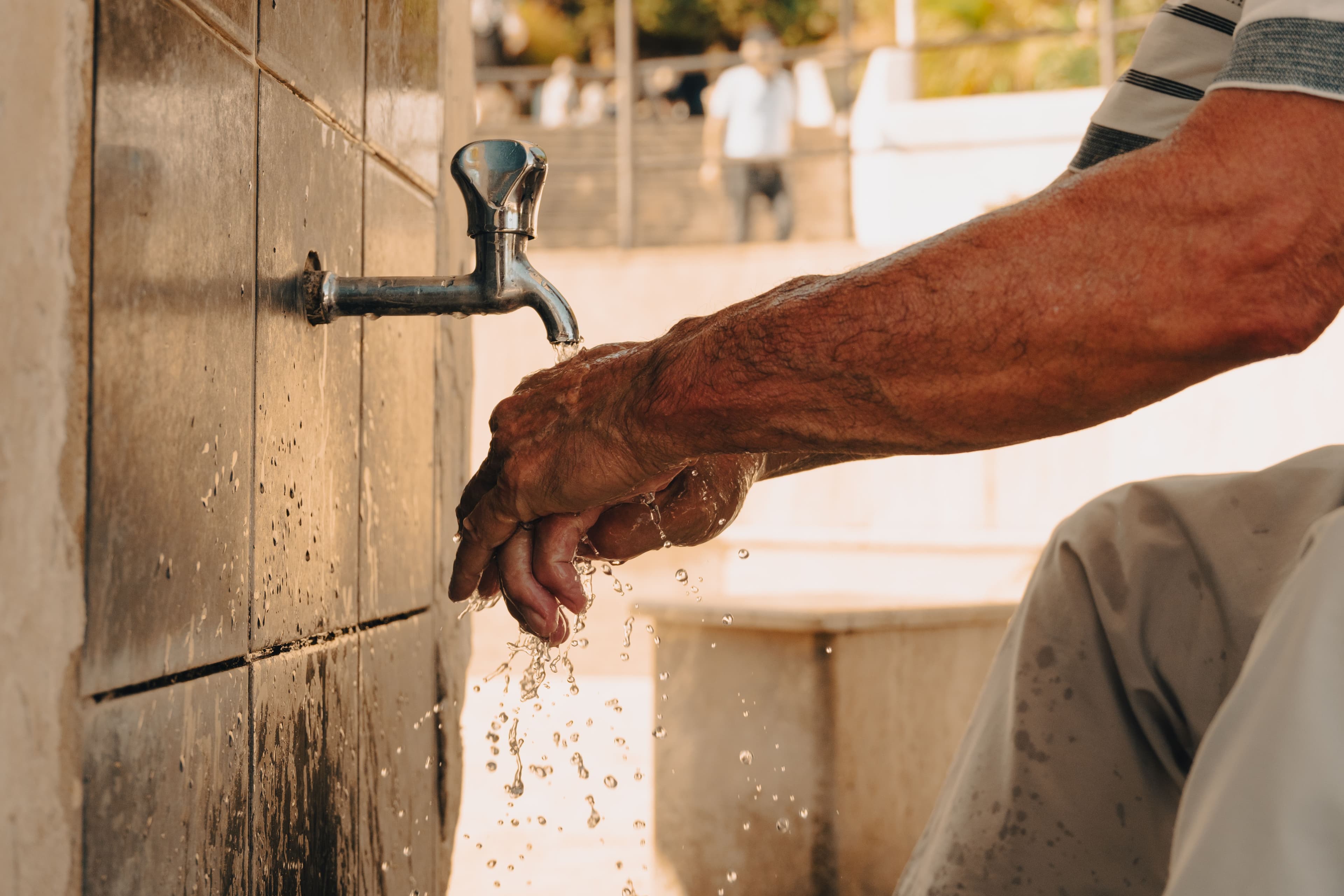 Close-up of hands being washed under a tap at an outdoor ablution area