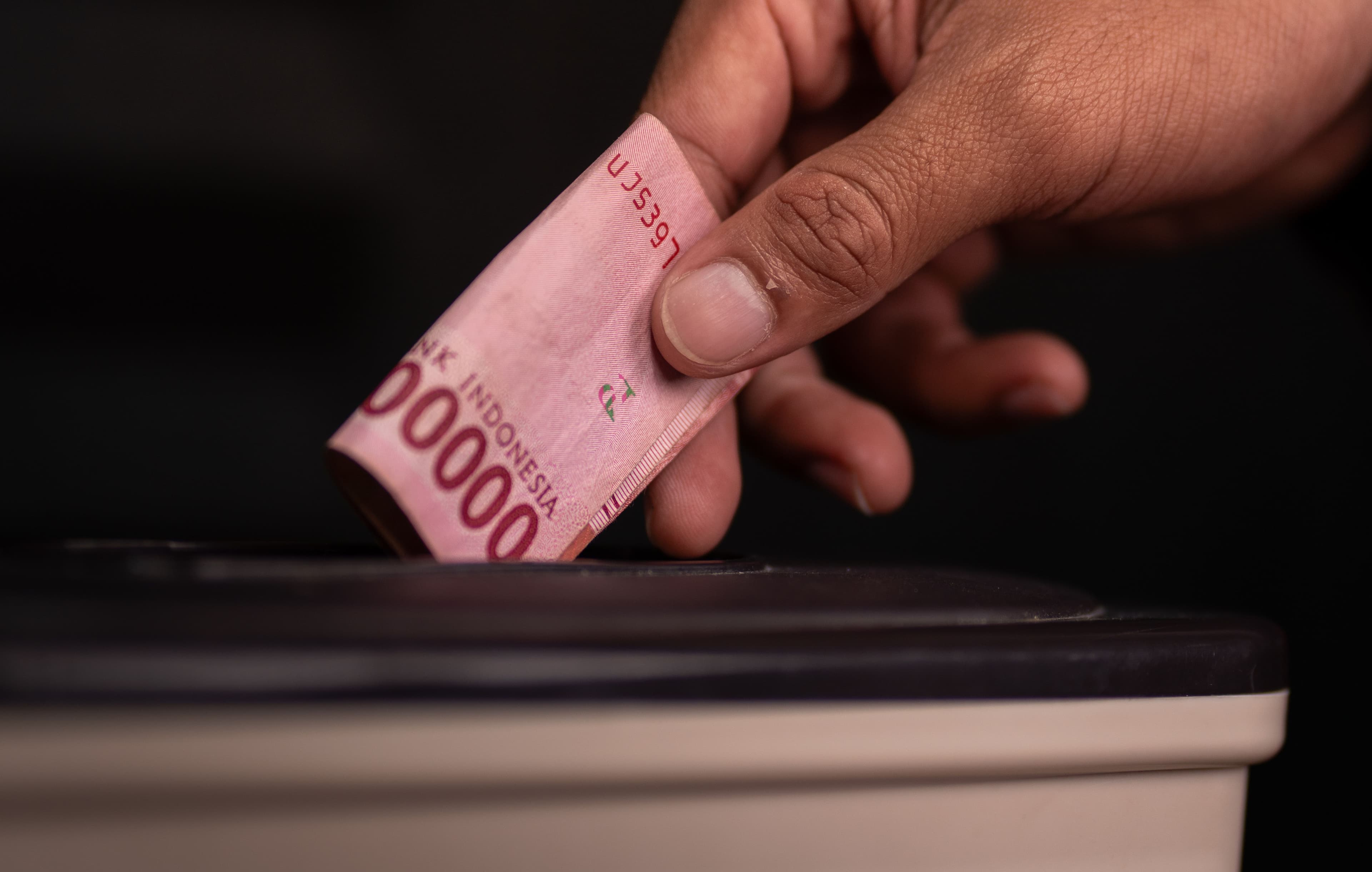 A hand placing a banknote into the slot of a donation box